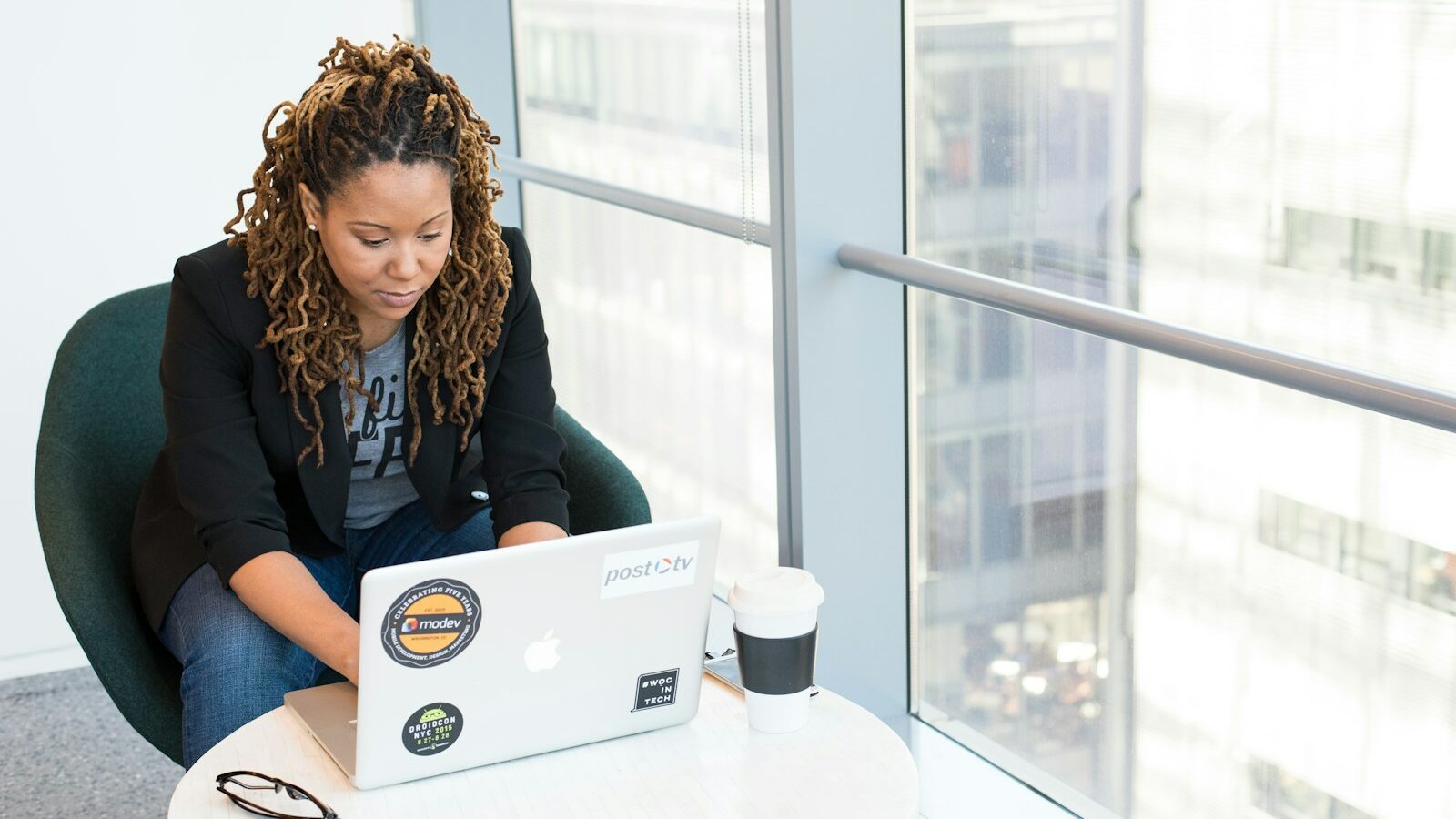 woman sits on padded chair while using MacBook during daytime